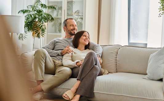 A man and a woman are sitting on a couch, holding hands and smiling at each other at Marcola Apartment Homes, Forest Grove