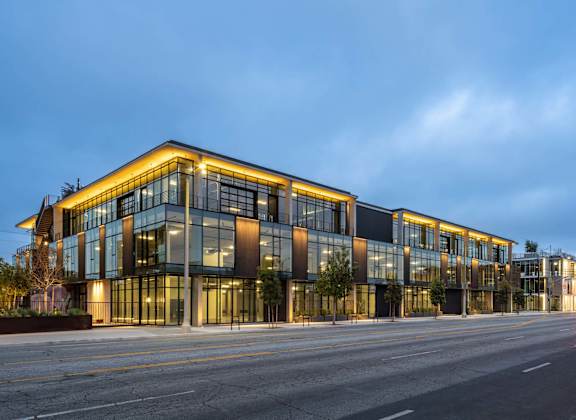 A modern building with a glass facade is illuminated from within and surrounded by a dark sky.