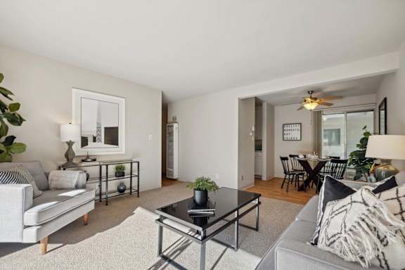 A living room with a grey couch, a black coffee table, and a dining area in the background.