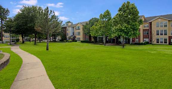 A grassy area with a walkway and trees in front of apartment buildings.