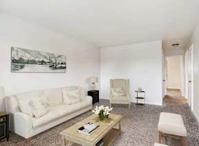 A living room with a white couch, a chair, a coffee table, and a painting on the wall.