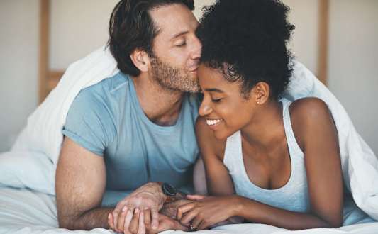 A man and a woman are sitting on a couch, holding hands and smiling at each other.