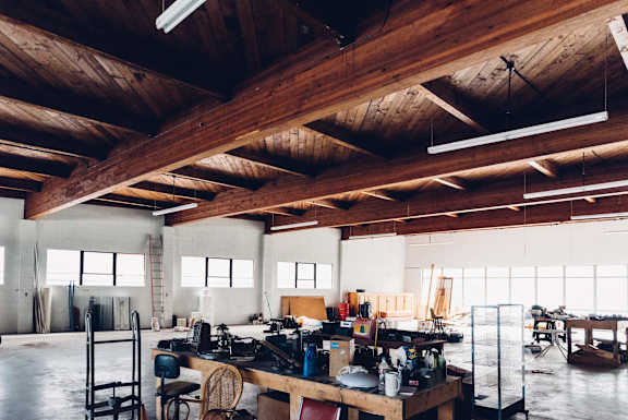 A workshop with wooden beams on the ceiling and various tools and equipment on the tables.