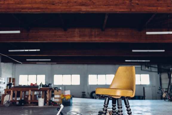 A yellow chair with wooden legs sits in a room with a wooden ceiling and walls.