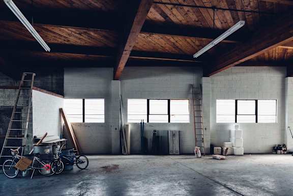 A large, empty warehouse with a ladder, a bicycle, and some construction materials.
