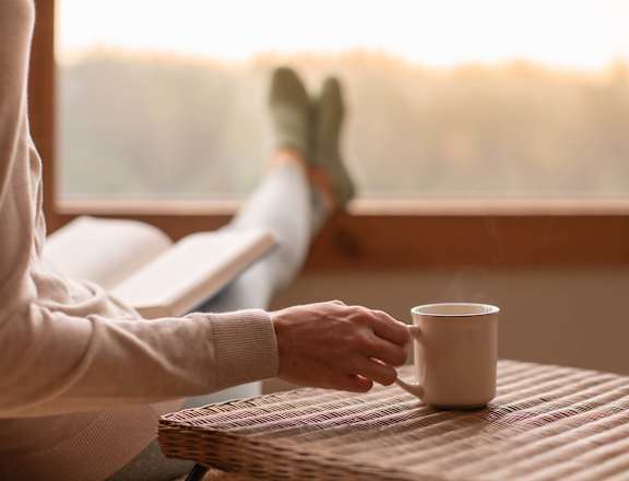 A person is holding a cup in their hand while sitting by a window.