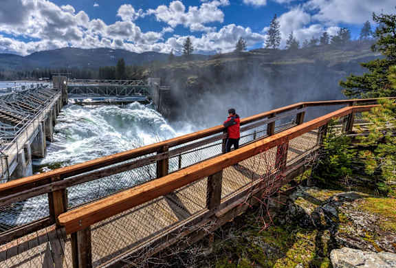 A person is standing on a wooden bridge over a river.