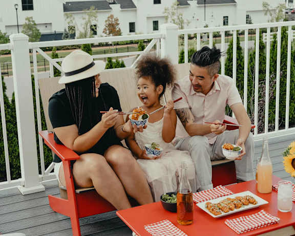 Three people are sitting on a red chair eating food.