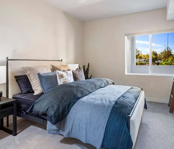 A bedroom with a large bed and a window showing a view of trees and a parking lot. at Casa Mira View Apartments, San Diego, CA 92126