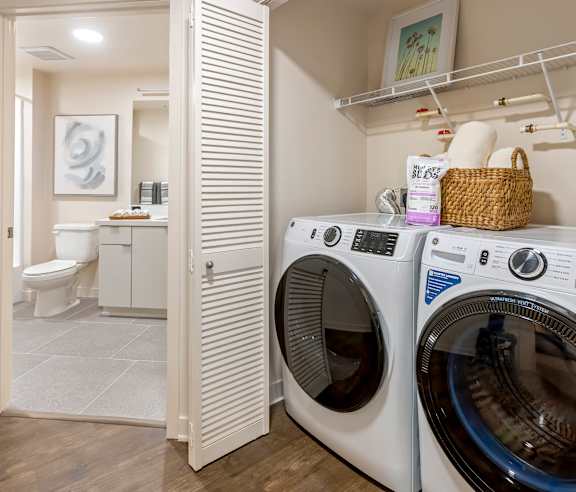 A white washing machine is in a laundry room with a basket of items on top of it. at Casa Mira View Apartments, San Diego, CA 92126