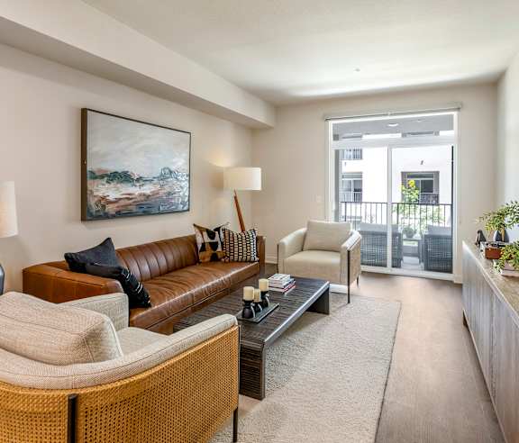 A living room with a brown leather couch, a wicker chair, and a painting on the wall. at Casa Mira View Apartments, San Diego, CA 92126