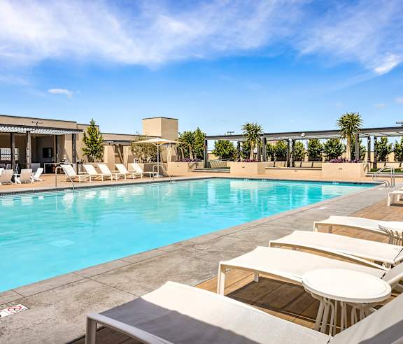 A pool with sun loungers and a building in the background. at Casa Mira View Apartments, San Diego, CA 92126