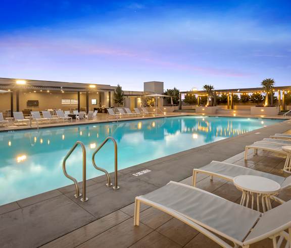 A poolside area with sun loungers and a pool at dusk. at Casa Mira View Apartments, San Diego, CA 92126