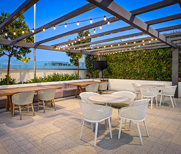 A patio with white chairs and tables under a pergola. at Elements Apartments, Irvine, CA