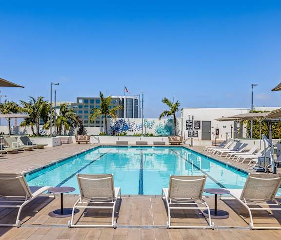 A pool with chairs around it and a building in the background. at Elements Apartments, Irvine, CA
