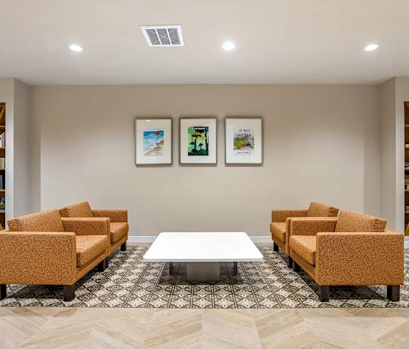 A waiting room with a patterned carpet and a row of orange chairs. at Elements Apartments, Irvine, CA