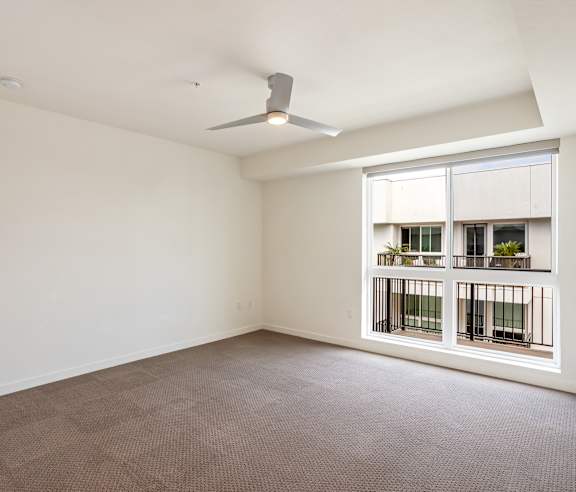 A room with a ceiling fan and a window with a view of a balcony. at Elements Apartments, Irvine, CA