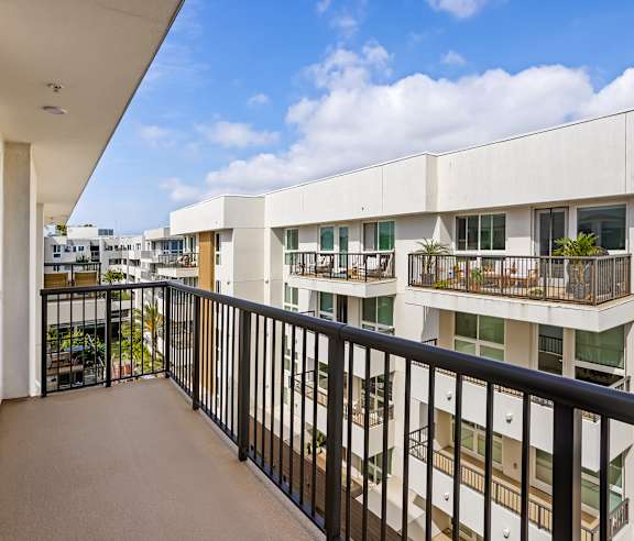 A balcony with a black railing overlooks a white building and a blue sky with clouds. at Elements Apartments, Irvine, CA