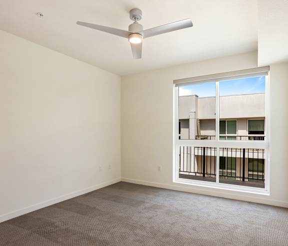 A room with a ceiling fan and a window overlooking a balcony. at Elements Apartments, Irvine, CA