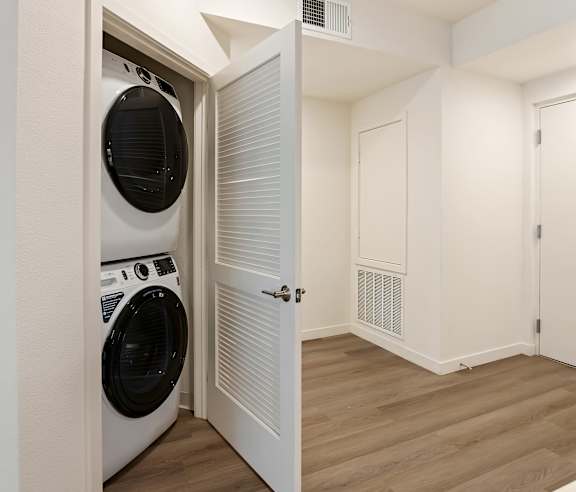 A white door is open to a laundry room with a washer and dryer. at Elements Apartments, Irvine, CA