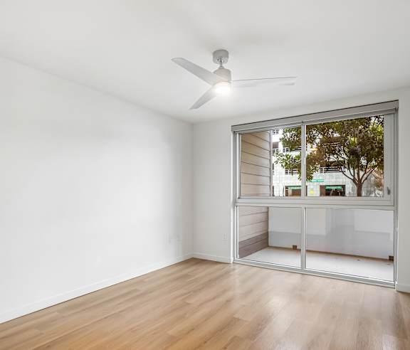 A room with a ceiling fan and a window overlooking a street. at Elements Apartments, Irvine, CA