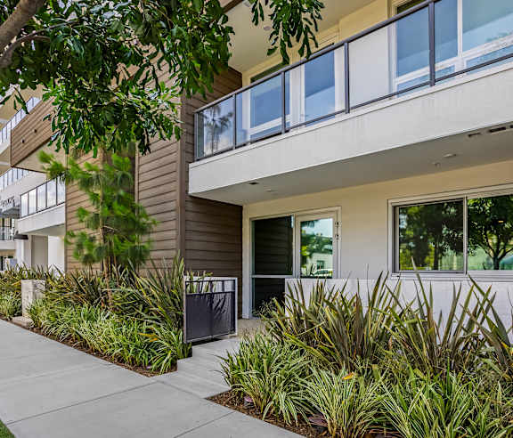 A modern building with a balcony and a green plant in front. at Elements Apartments, Irvine, CA
