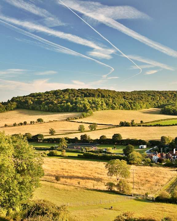 A rural landscape with a clear sky and contrails from planes.