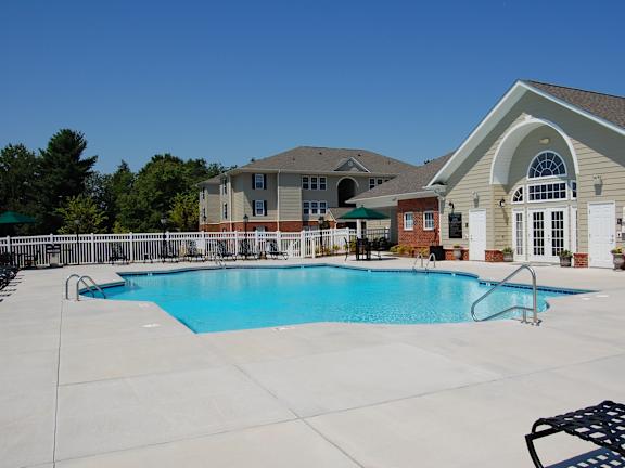 A large swimming pool in front of a building with a white fence and trees in the background.
