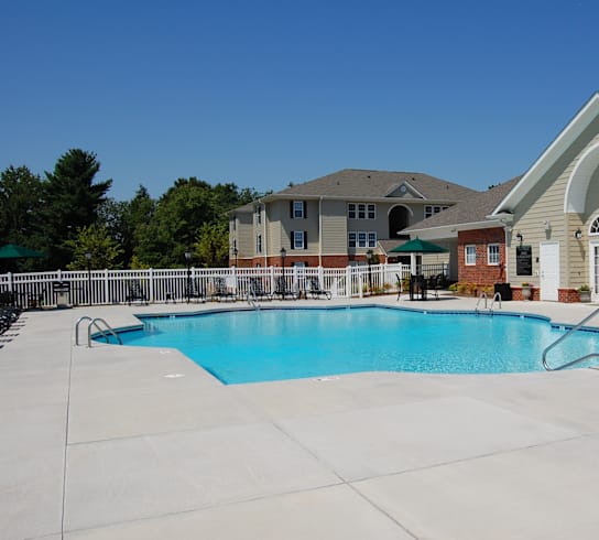 A large swimming pool in front of a building with a white fence and trees in the background.