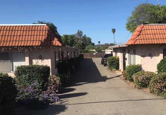 a driveway in front of two cottages with red tile roofs