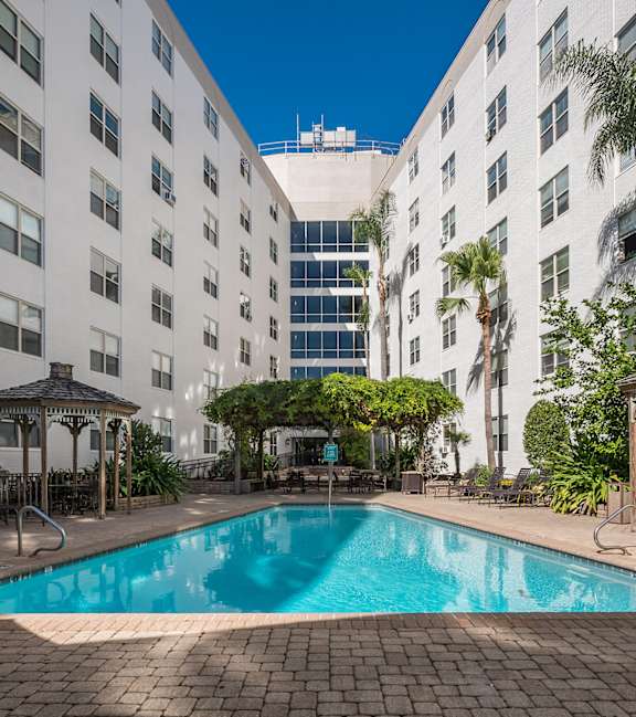 A swimming pool is surrounded by palm trees and a gazebo.