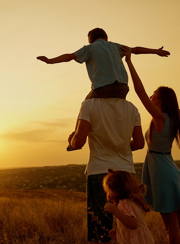 A family of three is playing in a field at sunset.