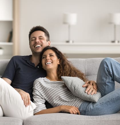 A man and a woman are sitting on a grey couch.