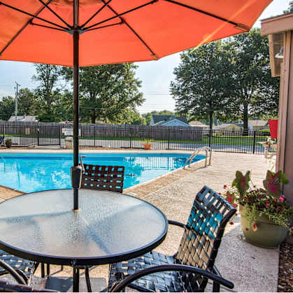 A table with chairs and an umbrella is set up by a pool.