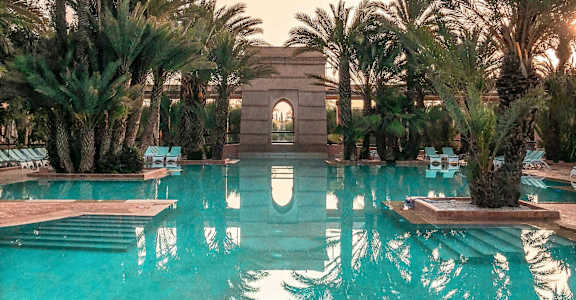 A pool surrounded by palm trees and a building in the background.