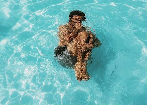 A person is floating in a pool with clear blue water.