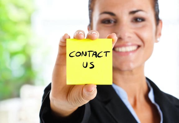 a woman holding up a yellow paper with contact us written on it