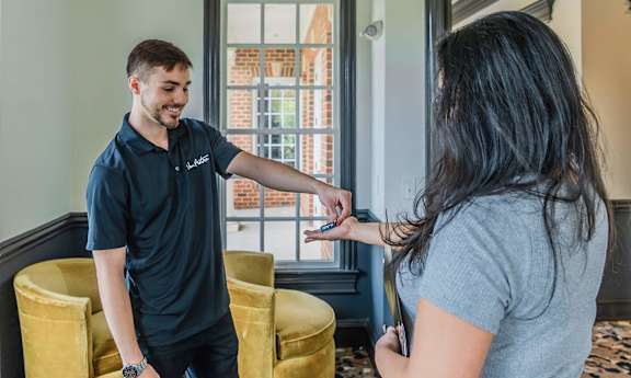 A man in a blue shirt is handing a key to a woman in a grey shirt. at Lakes Edge Apartments, North Carolina, 27409