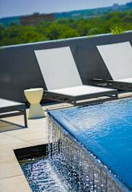 A pool with a waterfall and two lounge chairs.