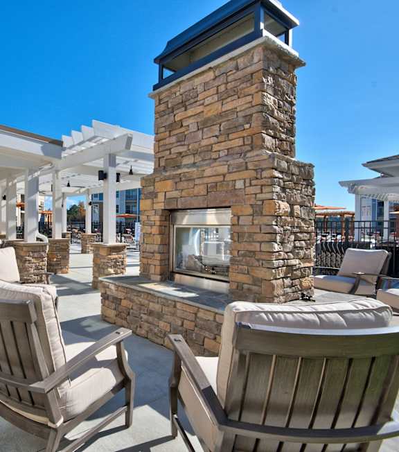 An outdoor brick fireplace area with chairs at Parkstone at Knightdale apartments in Knightdale, NC.