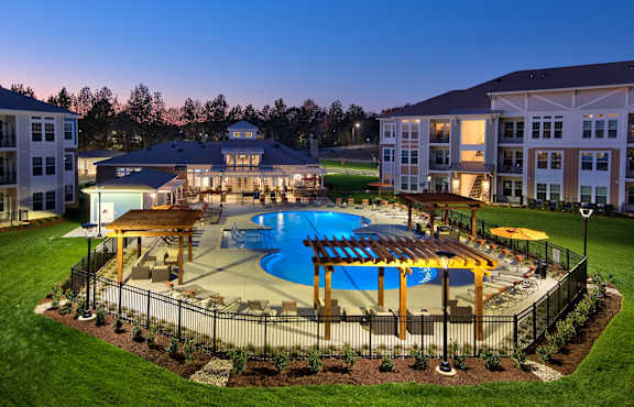 A large swimming pool surrounded by a fence and a gazebo in the middle of a grassy area at Parkstone at Knightdale apartments in Knightdale, NC. 
