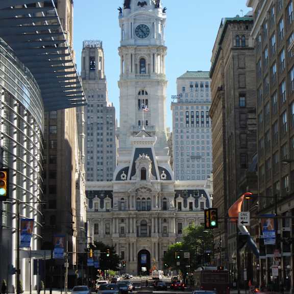 A large white building with a clock tower stands in the middle of a busy city street.