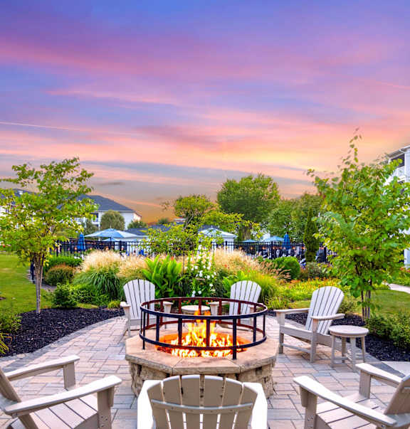 A backyard with a fire pit surrounded by chairs and trees.