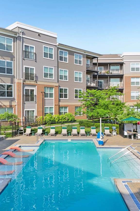 A large swimming pool surrounded by lounge chairs and apartment buildings.