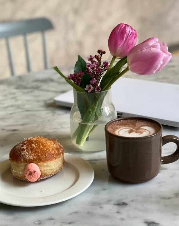 a cup of coffee and a donut on a table with tulips and a