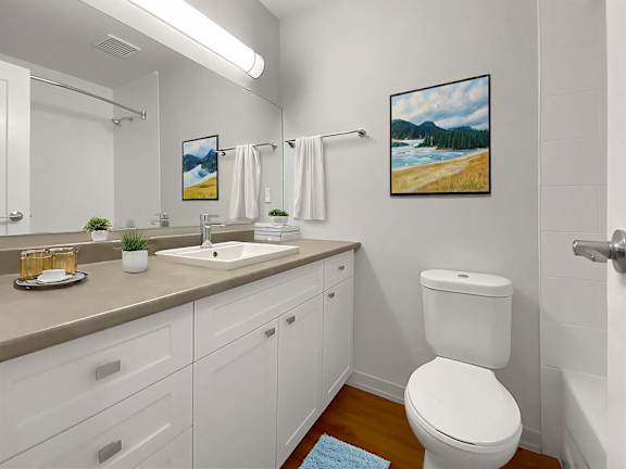 A bathroom with a white toilet, a sink, and a painting of a beach scene on the wall.