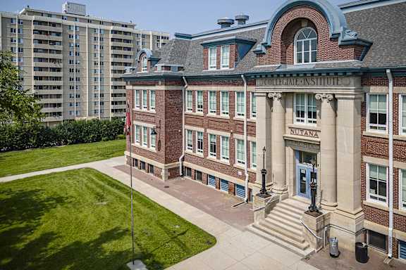 a brick building with a green lawn and an apartment building behind it