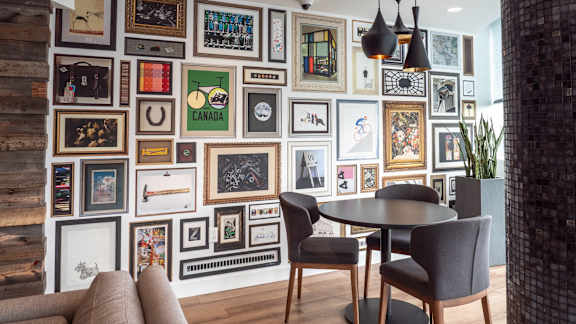 A wall of framed pictures in a room with a table and chairs.