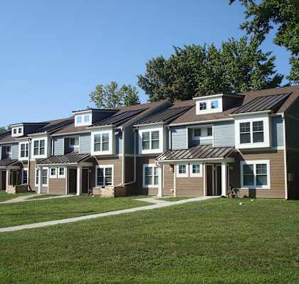 a row of houses on a grassy hill with trees in the background
