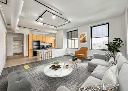 A living room with a grey couch, a white coffee table, and a yellow chair at The Des Moines Building Apartments, IA, 50309